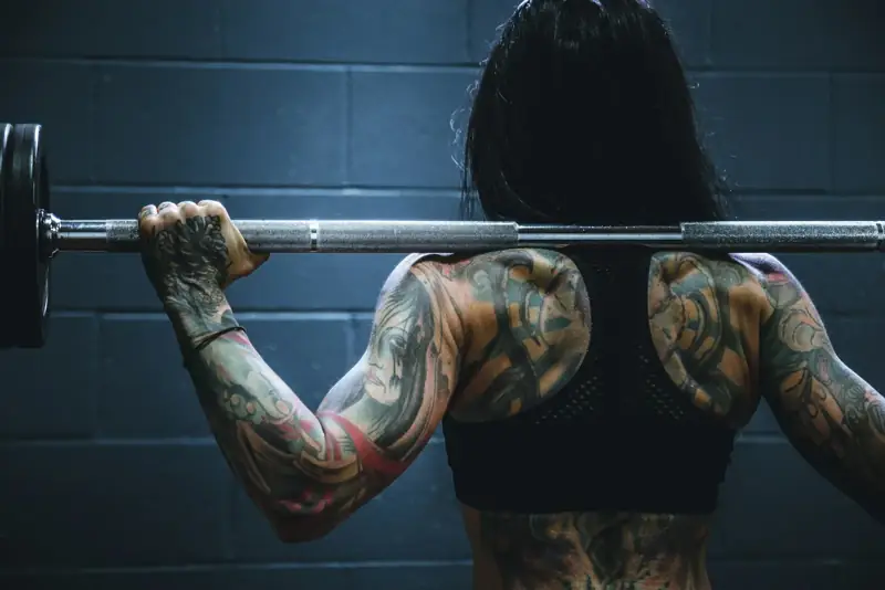 Mujer con tatuajes haciendo sentadilla con barra